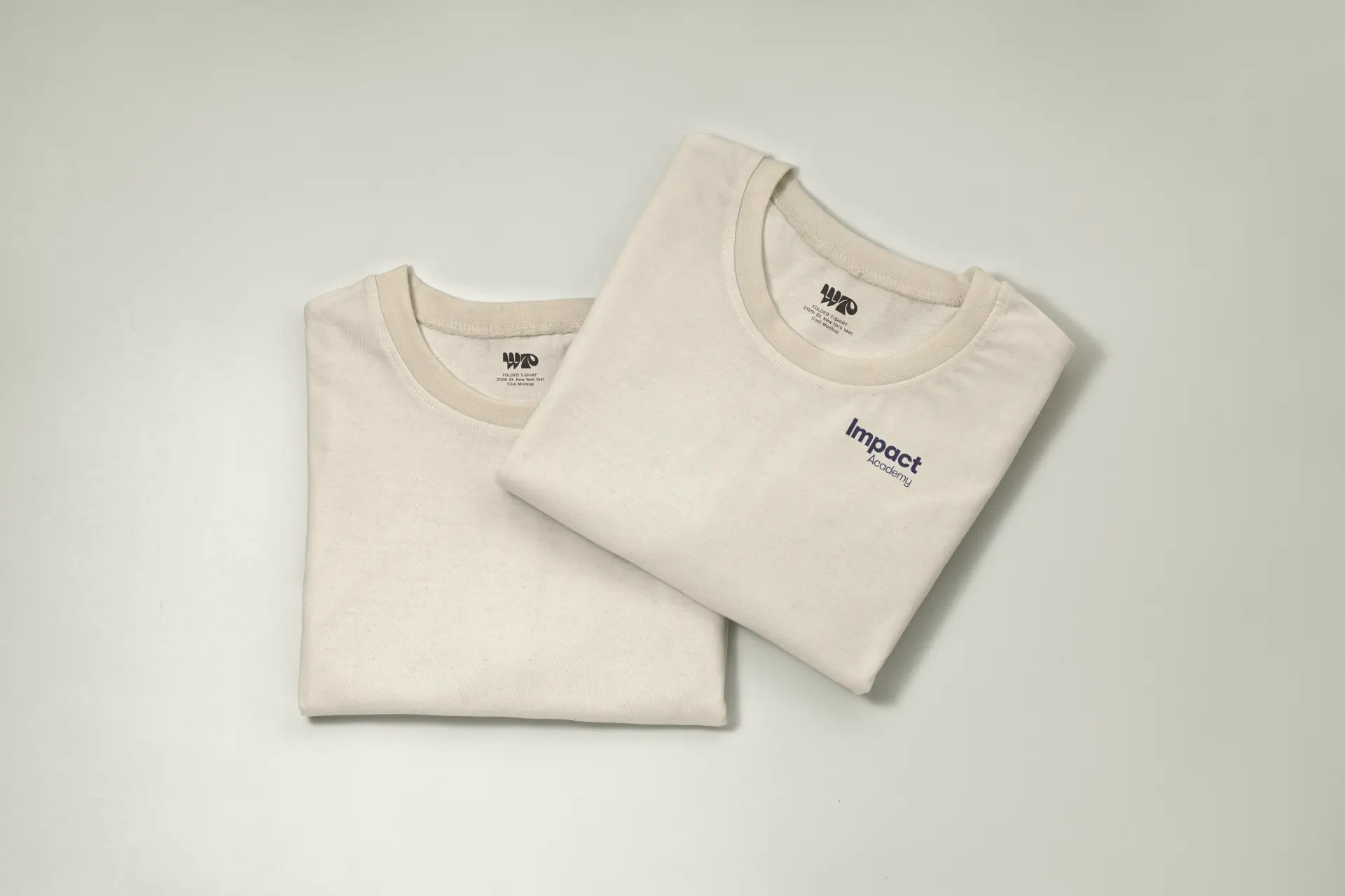 Two folded natural Impact Academy t-shirts with a small navy chest logo.